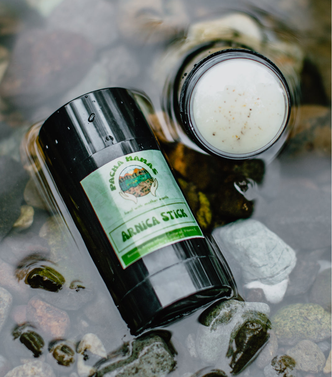 Bachara Baba Arnica Stick bottle on a natural background with water and stones.